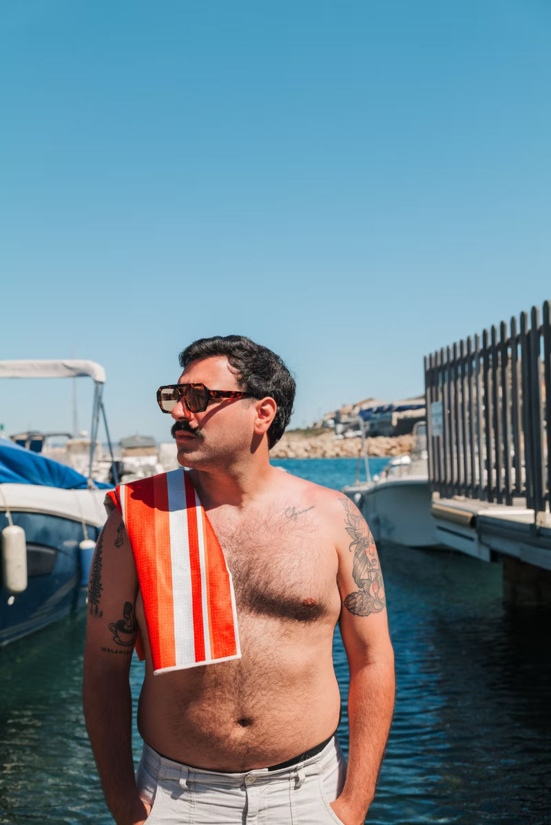 orange and white stripe towel on man shoulder by the water