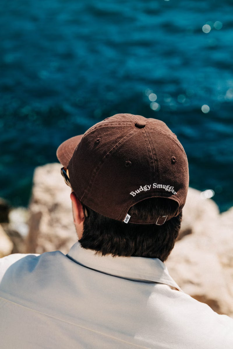 Brown hat with white text on a man y the water 
