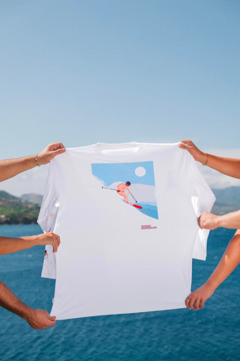 White tee with ski print held up by hands over the water 