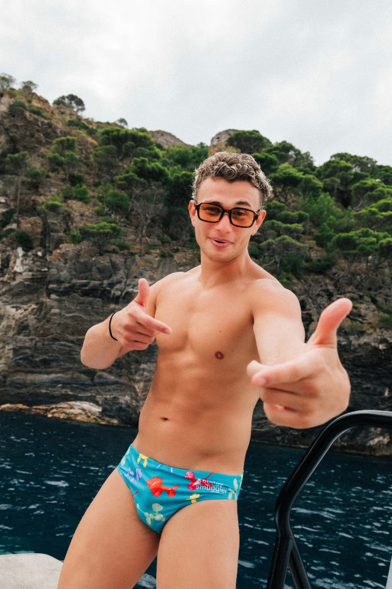 Man wearing blue swimwear briefs with dogs by the water 
