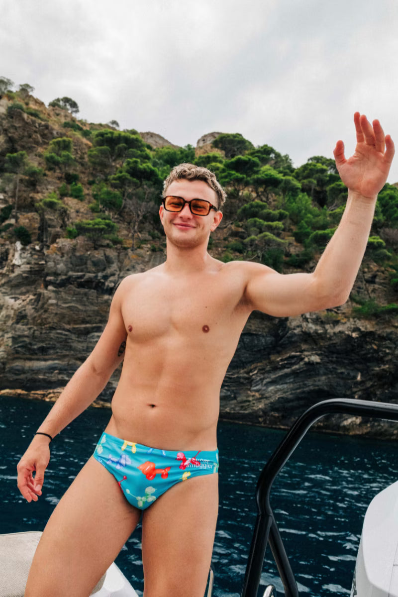 Man wearing blue swimwear briefs with dogs by the water 