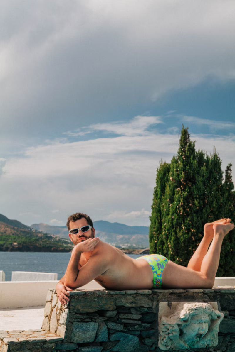 Man wearing green swimwear with crocodiles on them by the water 