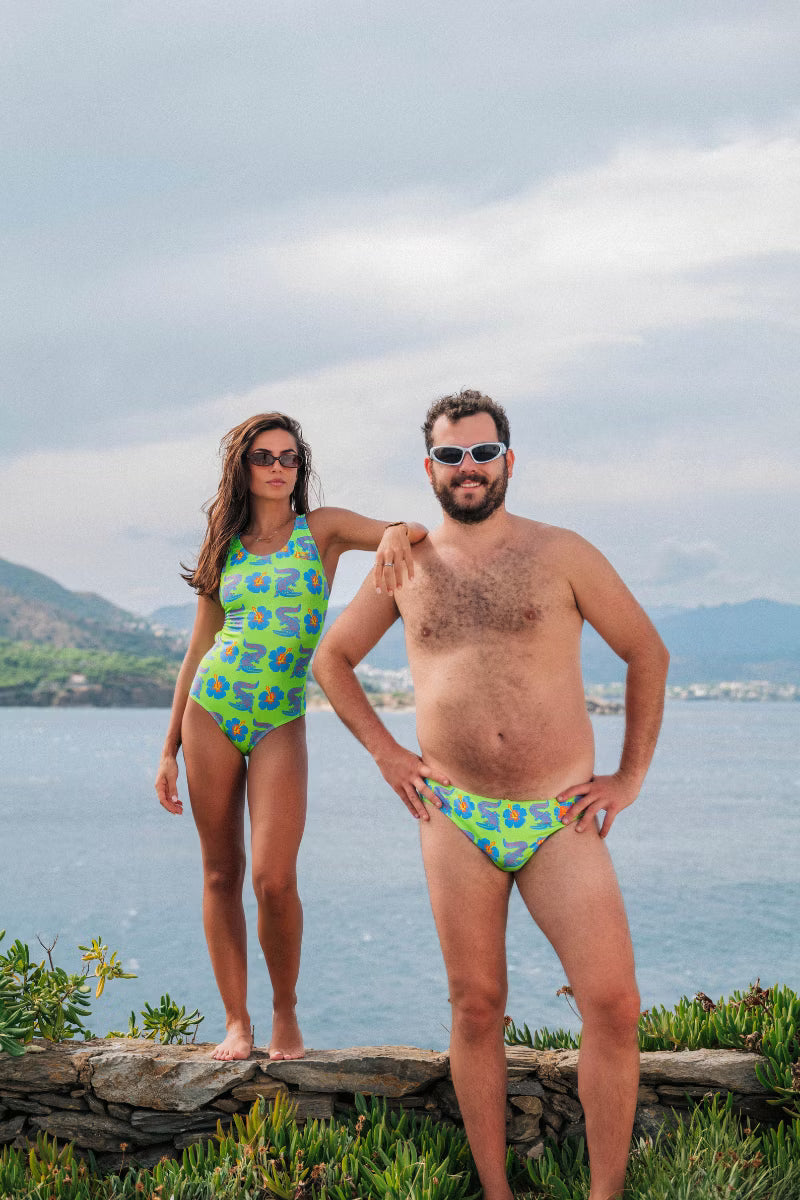 Man and women wearing green swimwear with crocodiles on them by the water 